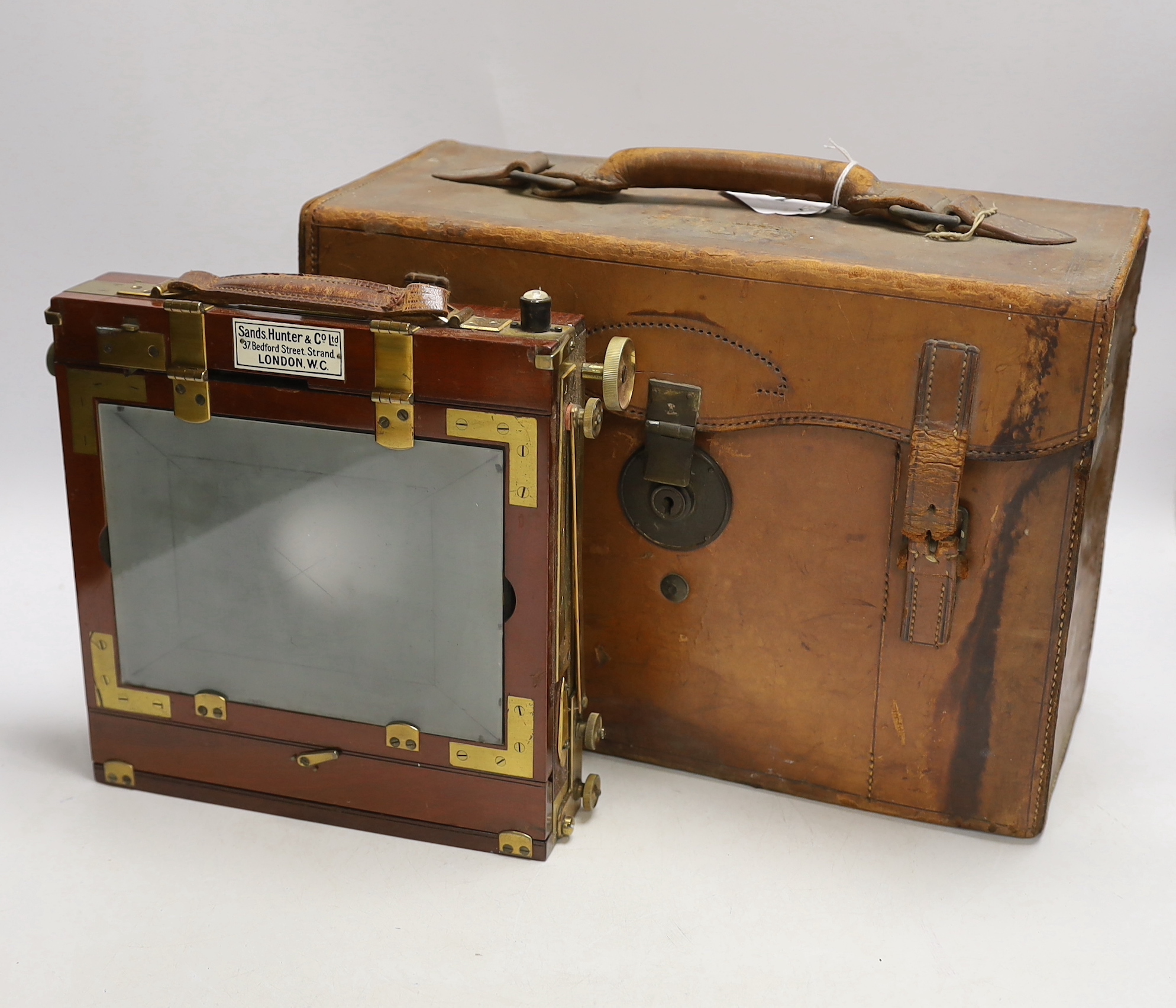 An early 20th century half plate camera by Sands, Hunter & Co. 37 Bedford Street, Strand, London WC, mahogany and brass frame, body 21 x 20cm, in the original leather case, also containing a Taylor, Taylor & Hobson Ltd.